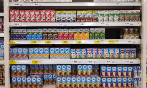 A well-stocked grocery store aisle with subtle gaps forming on the shelves—not empty, but clearly less abundant than expected